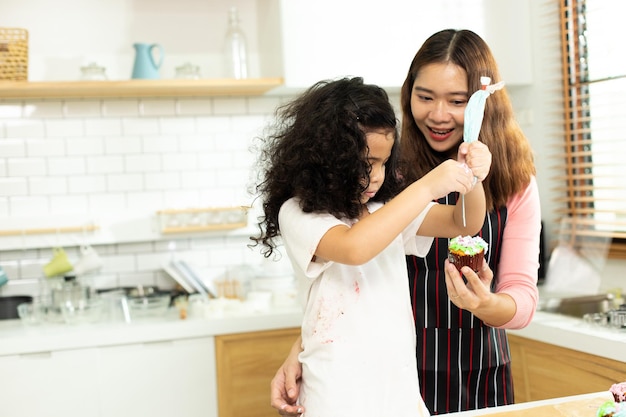 Asiatique Préscolaire Africain Arabe enfant personne faire un gâteau cuisiner dans la cuisine Mère préparer la décoration jolie avec plaisir éduquer sur le petit gâteau pour l'anniversaire soeur Crème gâchis sur tout le visage se sentir heureux espace de copie