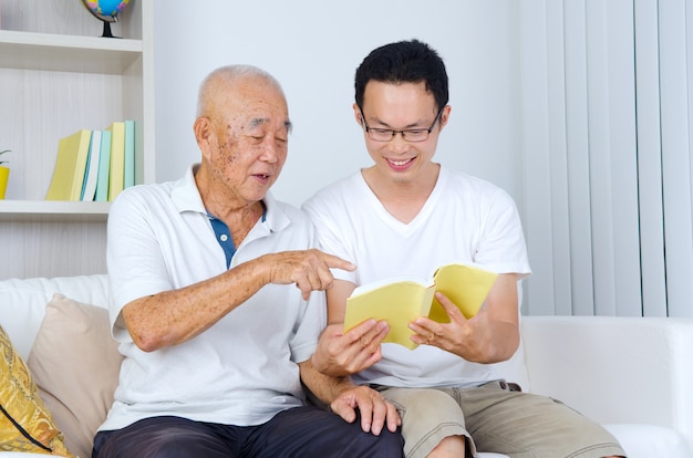 Asiatique senior homme lisant un livre avec son fils à la maison