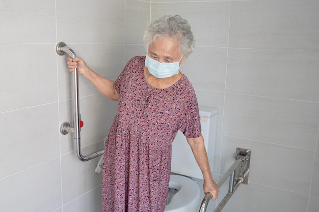 Asiatique senior ou vieille dame âgée femme patient utiliser toilettes salle de bain poignée sécurité dans l'hôpital de soins infirmiers sain concept médical fort