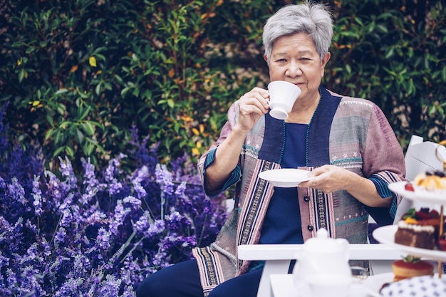 Asiatique vieille femme aînée âgée âgée buvant du thé au café dans un jardin de fleurs de lavande