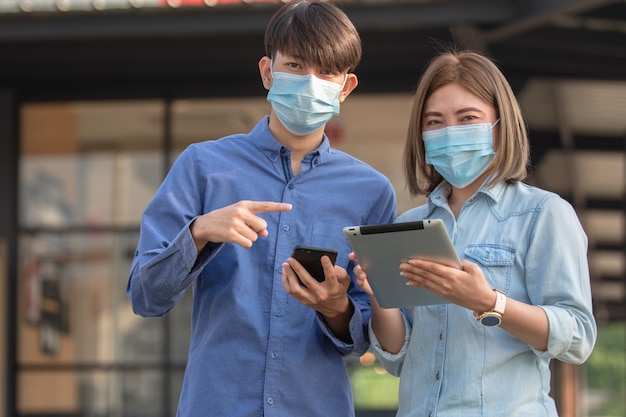 Les Asiatiques portent un masque facial et utilisent un smartphone à l'extérieur