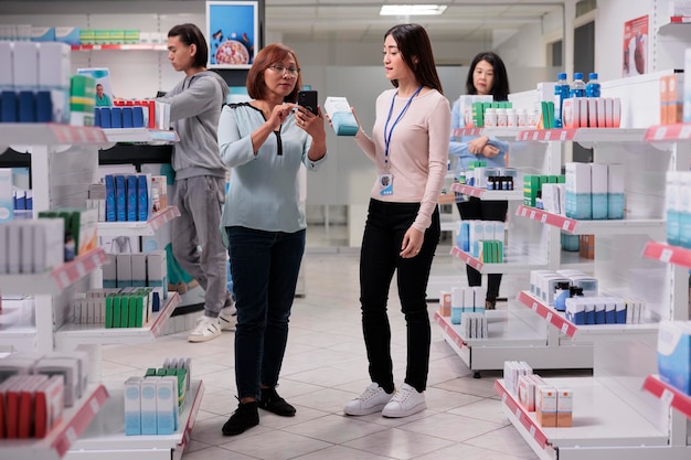 Les Asiatiques regardent un smartphone pour trouver des produits pharmaceutiques et des traitements médicaux en pharmacie. Spécialiste de la santé donnant une boîte de médicaments au client en magasin avec des suppléments et des vitamines.