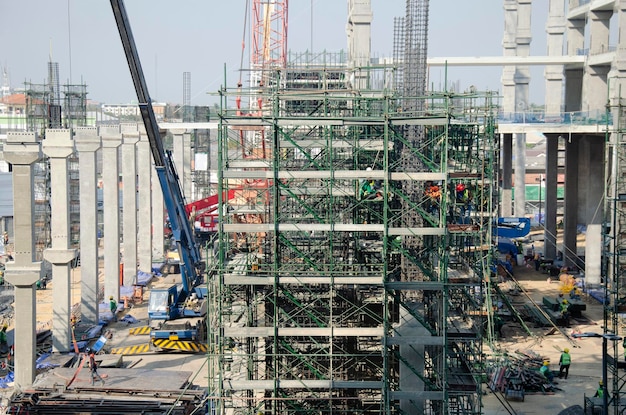 Les asiatiques et les travailleurs thaïlandais avec de la machinerie lourde travaillant un nouveau bâtiment sur le site de construction d'un immeuble de grande hauteur sur un échafaudage dans la capitale de Bangkok en Thaïlande