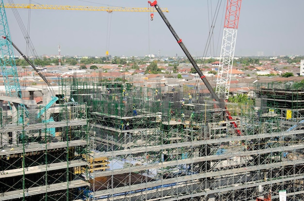 Les asiatiques et les travailleurs thaïlandais avec de la machinerie lourde travaillant un nouveau bâtiment sur le site de construction d'un immeuble de grande hauteur sur un échafaudage dans la capitale de Bangkok en Thaïlande