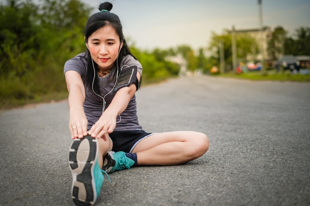 Asie belle femme en articles de sport se réchauffer avant de courir sur la route.