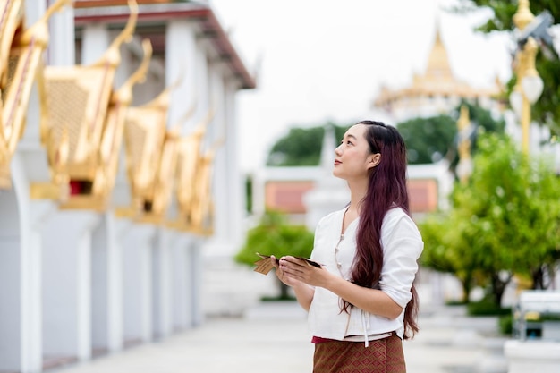 Photo asie femme vêtue d'un costume traditionnel de thaïlande à la recherche de temple et tenir l'ancien livre de tripitaka sanskrit du seigneur bouddha dhamma sanctuaire ratchanatdaram bangkok