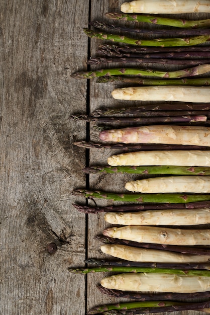 Asperges blanches, vertes et violettes sur planche de bois rustique