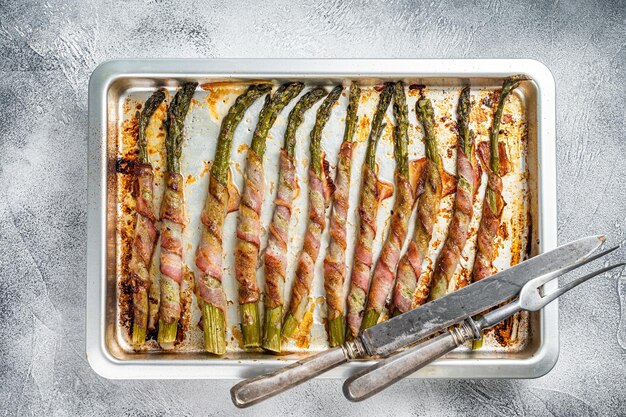 Asperges enveloppées de bacon sur un plateau de barbecue. Fond blanc. Vue de dessus.