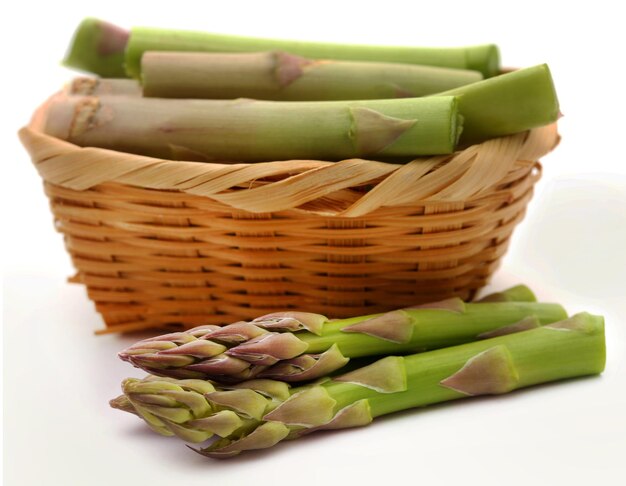 Asperges fraîches dans un panier sur fond blanc