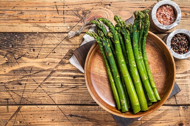 Asperges non cuites dans une assiette en bois. fond en bois. Vue de dessus. Espace de copie.