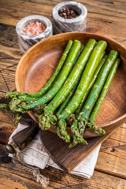 Asperges non cuites dans une assiette en bois. fond en bois. Vue de dessus.