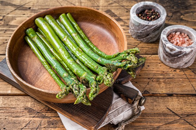 Asperges non cuites dans une assiette en bois. fond en bois. Vue de dessus.