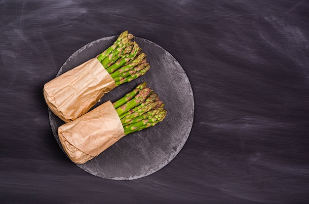 Photo asperges vertes dans un sac en papier sur une ardoise sur fond noir. récolte saisonnière de printemps. mise à plat, espace de copie. concept d'alimentation saine. vue d'en-haut.