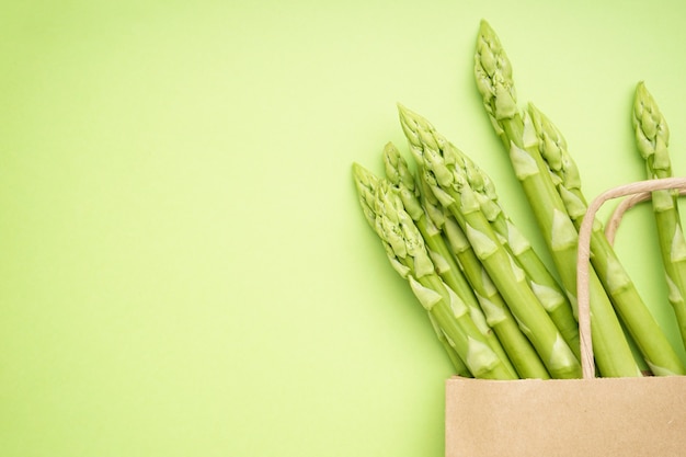 Asperges vertes dans un sac en papier sur une surface vert clair, place pour le texte. Fermer