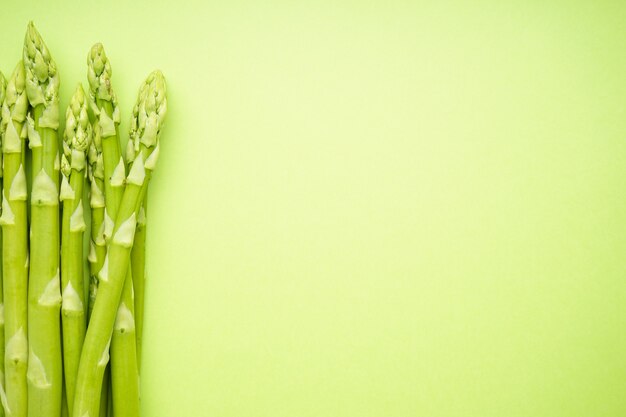 Asperges vertes fraîches sur une surface vert clair, espace pour le texte. Mise à plat.