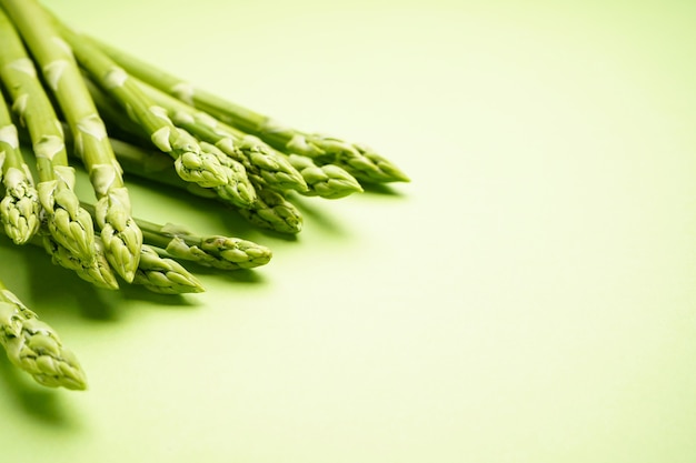 Asperges vertes fraîches sur une surface vert clair, espace pour le texte.