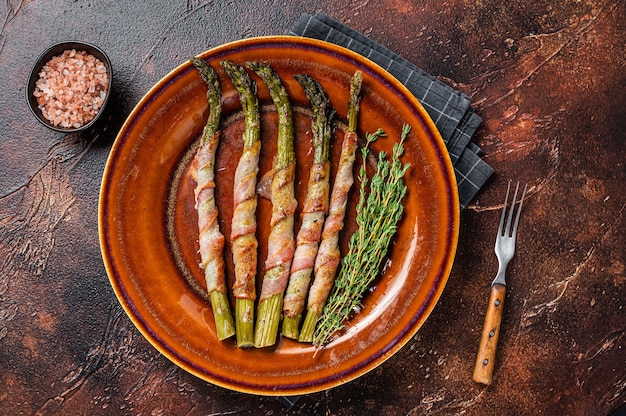 Asperges vertes grillées enveloppées de bacon sur une assiette. Fond sombre. Vue de dessus.