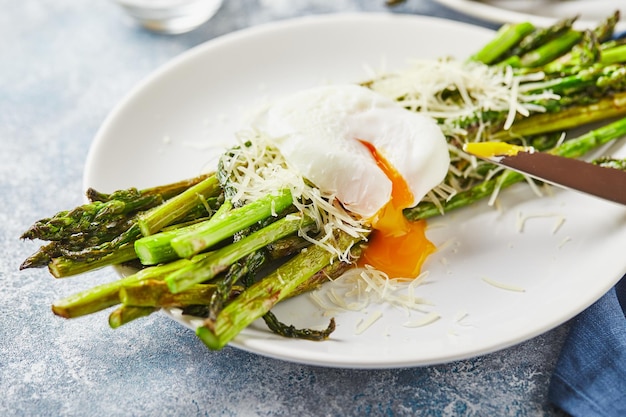 Asperges vertes avec œuf poché et petit-déjeuner végétarien au parmesan servi sur deux assiettes blanches sur fond clair