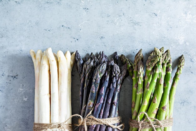 Asperges vertes violettes blanches brutes sur fond bleu Concept d'aliments crus