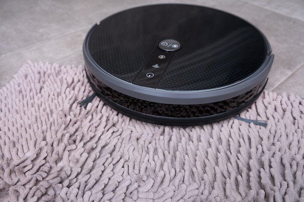 Aspirateur robot sur un tapis gris avec un gros plan de pile.