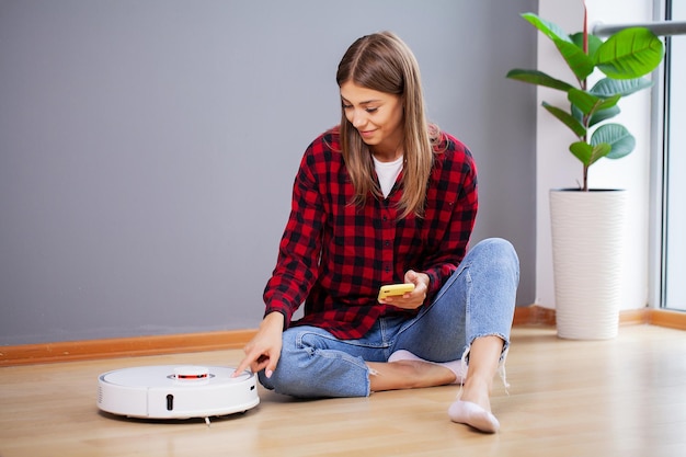 Aspirateur robotique blanc nettoyant le sol pendant qu'une femme assise près du mur et se repose