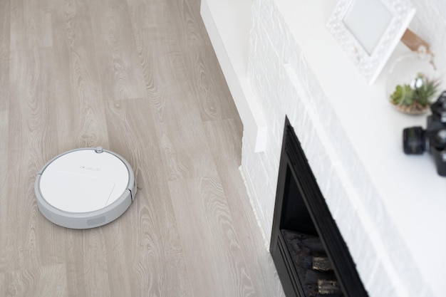 Aspirateur robotique blanc sur sol stratifié nettoyant la poussière à l'intérieur du salon. Technologie de ménage électronique intelligente.