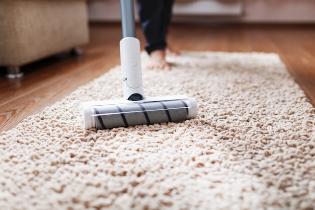 Un aspirateur sans fil nettoie la moquette du salon avec le bas des pieds.