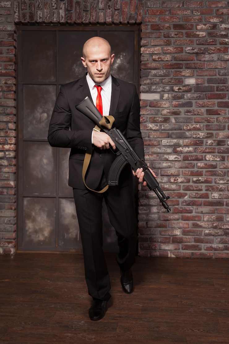 Photo assassin en costume et cravate rouge tenant une mitrailleuse