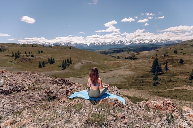 Asseyez-vous dans la position du lotus au milieu du paysage montagneux de la forêt et méditez. Une jeune fille brune en tenue de sport est assise sur un tapis et se concentre.