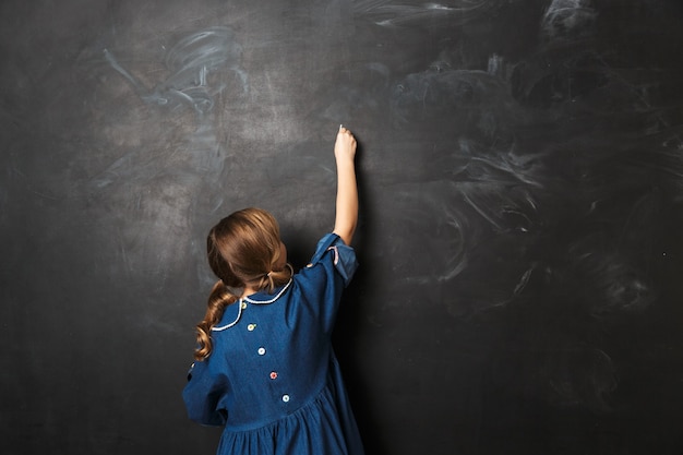 assez heureuse jeune petite écolière posant isolée sur le mur du mur du tableau.