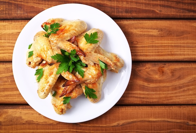 Assiette avec ailes de poulet au four et persil sur un fond en bois. Vue de dessus