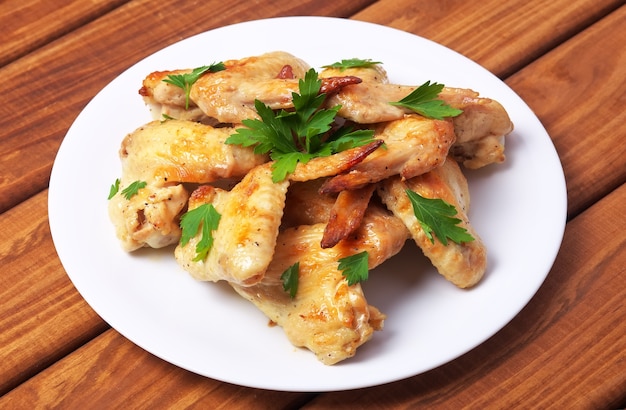 Assiette avec ailes de poulet au four et persil sur un fond en bois.