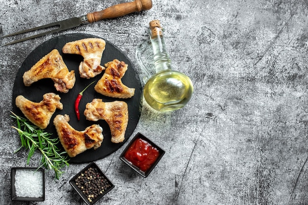 Une assiette d'ailes de poulet avec une bouteille de poivron rouge sur le côté.