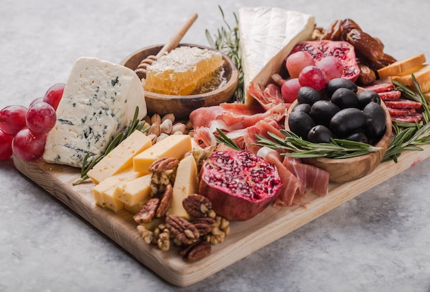 Assiette Antipasti Italienne Traditionnelle. Fromages Assortis Sur Planche à Découper En Bois. Fromage Brie, Tranches De Cheddar, Gogonzola, Raisins De Noix, Olives, Prosciutto, Romarin Et Verre De Vin Rouge. Vue De Dessus