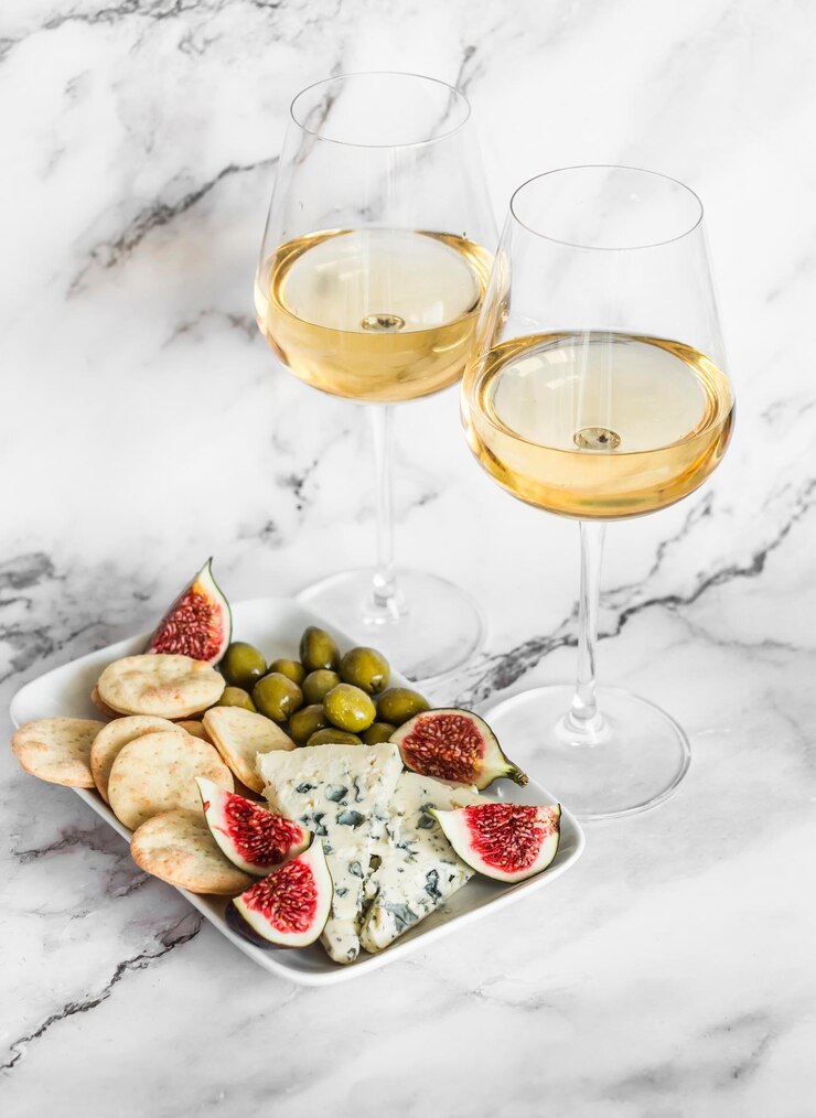 Photo assiette d'apéritif avec olives au fromage bleu craquelin au fromage fait maison figues et deux verres de vin blanc sur fond de marbre clair vue de dessus
