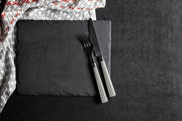 Assiette en ardoise noire avec fourchette et couteau et nappe