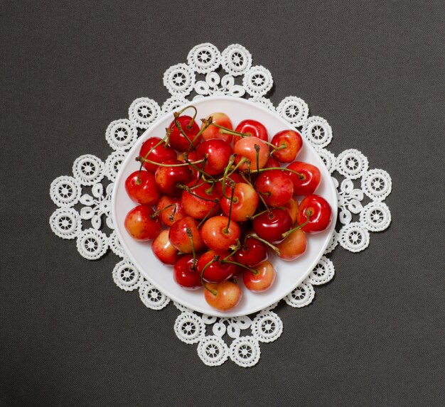 Assiette aux cerises sur une serviette en dentelle sur fond gris, vue d'en haut