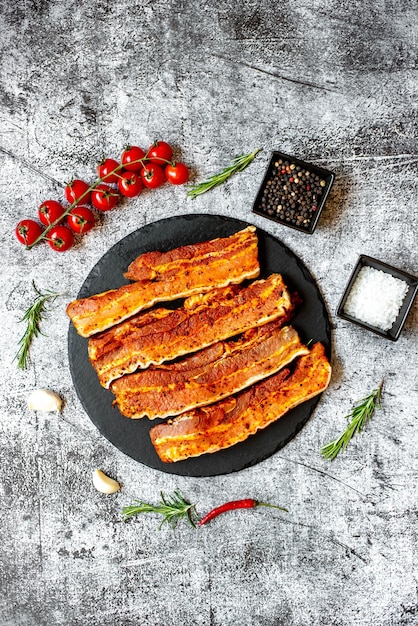 Une assiette de bacon avec tomates et ail sur fond gris.