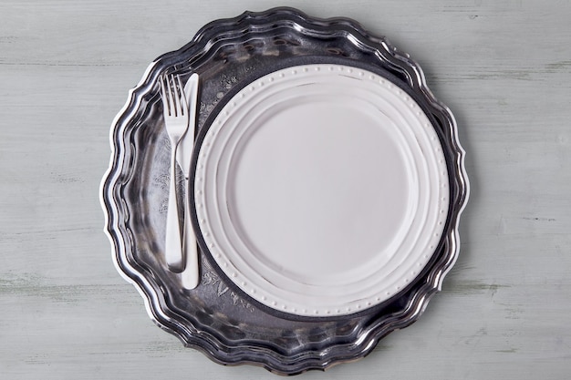 Assiette blanche avec couverts sur un plateau en métal brillant sur une table en bois clair Modèle de présentation des plats du menu