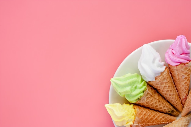 Assiette blanche de divers cônes de crème glacée sur fond rose pour desse douce et rafraîchissante