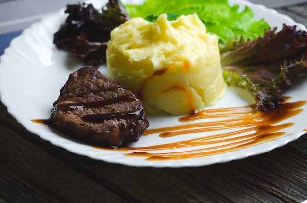 Sur une assiette blanche, sur un fond en bois, purée de pommes de terre à la viande de boeuf sauce balsamique magnifiquement polie