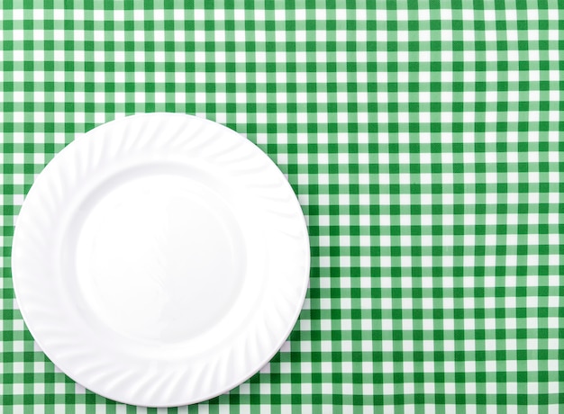 Assiette blanche sur fond de nappe en tissu à carreaux vert et blanc.