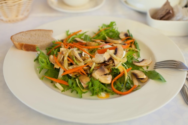 Assiette blanche avec fourchette, pain blanc et salade verte aux champignons et carottes dessus