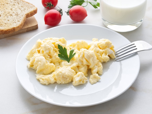 Assiette blanche avec des œufs brouillés poêlés sur un fond blanc clair avec des tomates. Omelette