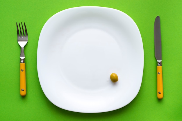 Assiette blanche avec une olive et couverts sur nappe verte