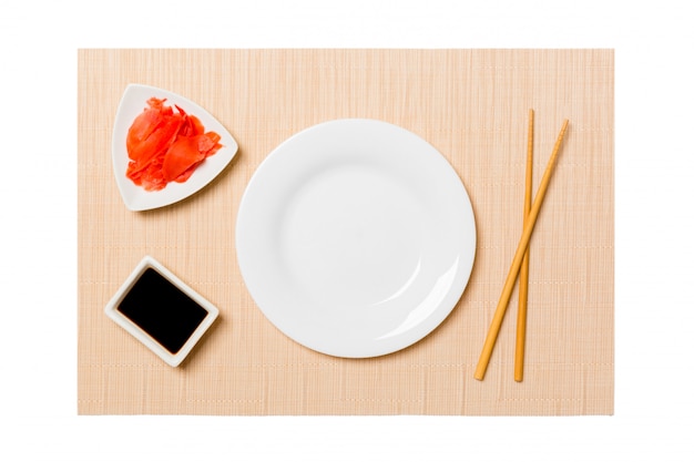 Assiette blanche ovale vide avec des baguettes pour sushi, gingembre et sauce soja sur fond de tapis de sushi brun