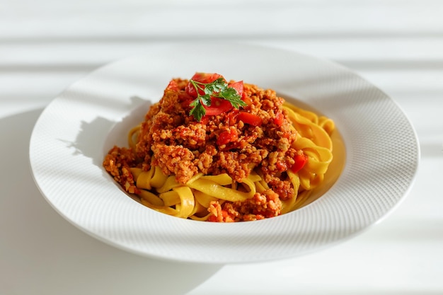 Assiette blanche avec pâtes bolognaises et feuille de persil sur le dessus debout sur la table. Préparation d'un repas italien traditionnel à partir de nouilles.