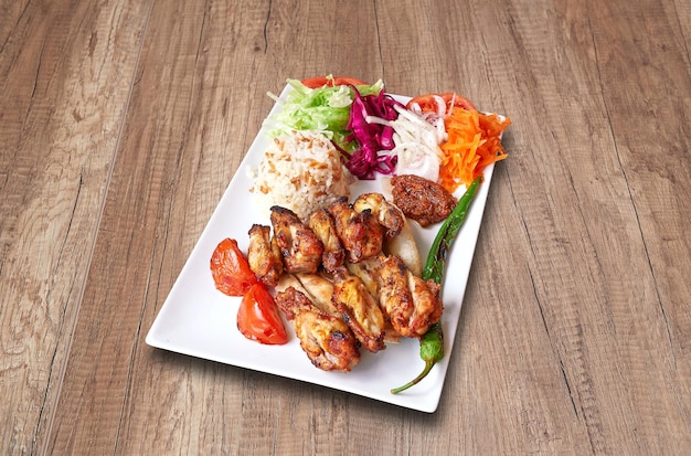 Assiette blanche avec pilons de poulet et légumes sur table en bois