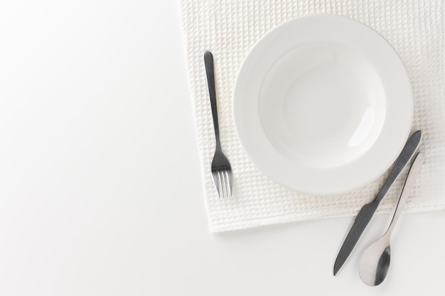 Une assiette blanche sur une table blanche avec des couverts placés Il n'y a pas de nourriture dans l'assiette. Équipement ménager