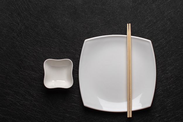 Assiette blanche vide avec des baguettes et une saucière sur une table sombre. Style de cuisine japonaise. Vue de dessus